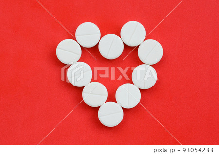 Several white tablets lie on a bright red background in the shape of a heart. Background image on medicine and pharmaceutical topics Several white tablets lie on a bright red background in the shape of a heart. Background image on medicine and pharmaceutical topics 93054233