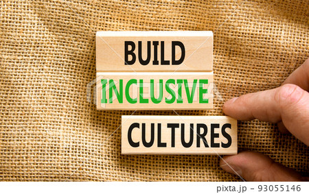 Build inclusive cultures symbol. Concept words Build inclusive cultures on wooden blocks. Businessman hand. Beautiful canvas background. Business build inclusive cultures concept. Copy space. 93055146