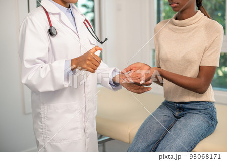 Doctor spraying sanitizer on hands of African American woman 93068171