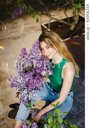 a blonde woman in a green top and jeans with lilac flowers.  93068259