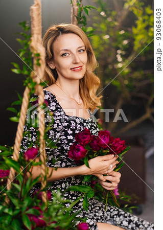 an attractive middle-aged blonde woman with flowers sits on a swing. 93068403