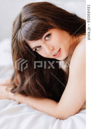 an attractive and sexy young woman with long dark hair lies in bed. bed linen. 93068491