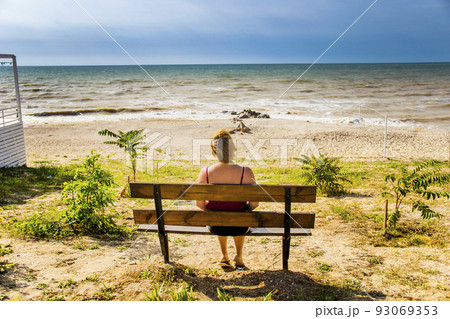 a woman sitting on the bench and looking at the sea 93069353