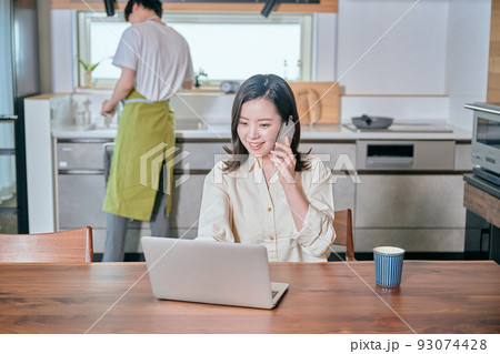 テレワークでスマホで電話をする女性と家事をする男性 93074428