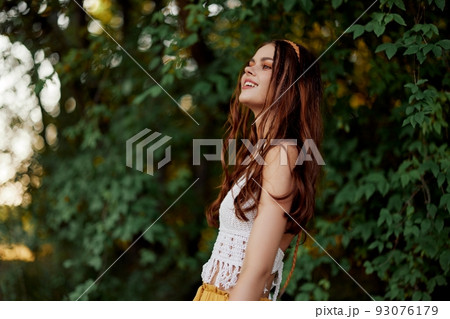 A woman in eco-friendly clothing in a hippie look dances in nature in the park and smiles at the world. The concept of harmony with the body and the surrounding nature A woman in eco-friendly clothing in a hippie look dances in nature in the park and smiles at the world. The concept of harmony with the body and the surrounding nature 93076179