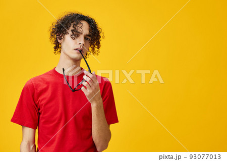 Incredulous myopic young student man in red t-shirt hold funny eyewear on teeth posing isolated on yellow studio background. The best offer with free place for advertising. Education College concept 93077013