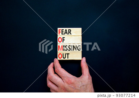 FOMO fear of missing out symbol. Concept words FOMO fear of missing out on wooden blocks on a beautiful black background. Businessman hand. Business FOMO fear of missing out concept. Copy space. 93077214