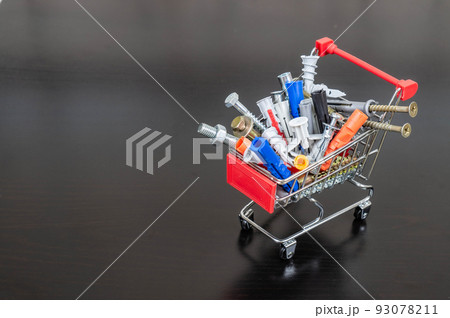 Different types of fasteners in a supermarket trolley. Place for text or logo. Concept: fastener store. Dark background. Different types of fasteners in a supermarket trolley. Place for text or logo. Concept: fastener store. Dark background. 93078211