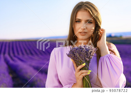 Young woman in dress holding bouquet of flowers standing in lavender field 93078722