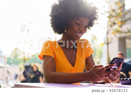 Happy afro woman using mobile phone at outdoor cafe Happy afro woman using mobile phone at outdoor cafe 93078725