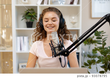 Young curly female recording podcast from home and talking into a microphone 93078795