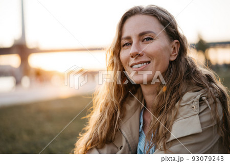 Happy young woman sitting on lawn outdoors in the city Happy young woman sitting on lawn outdoors in the city 93079243