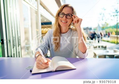 Casual woman sitting at table and taking notes in notebook .on the cafe terrace 93079318