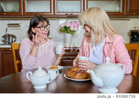 Friends two mature women drinking tea with cupcake in kitchen 93080756