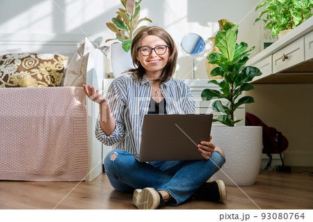 Mature woman sitting on the floor at home looking at laptop 93080764