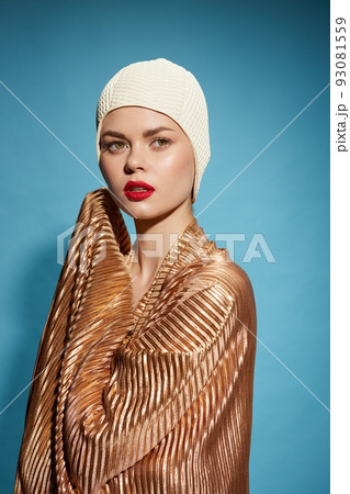 Goldfish concept. A girl with red lips in a gold scarf and a swimming cap looks away on a blue background 93081559