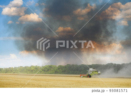 Combine harvester against the backdrop of black smoke rising into the sky. 93081571
