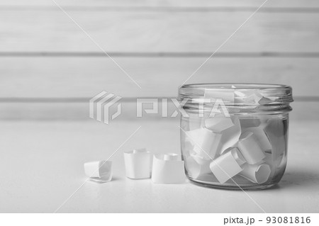 Glass jar with paper pieces on white table Glass jar with paper pieces on white table 93081816