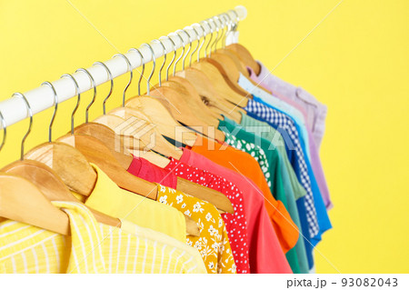 Bright clothes hanging on rack against yellow background, closeup. Rainbow colors Bright clothes hanging on rack against yellow background, closeup. Rainbow colors 93082043
