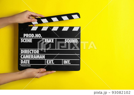Woman holding clapperboard on yellow background, closeup with space for text. Cinema production 93082102