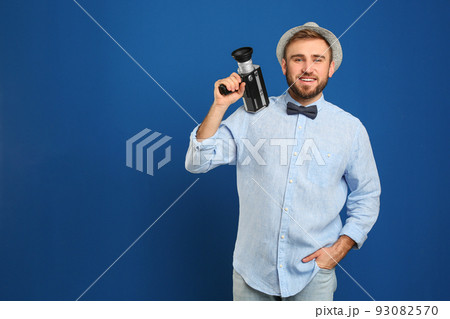 Young man with vintage video camera on blue background. Space for text 93082570