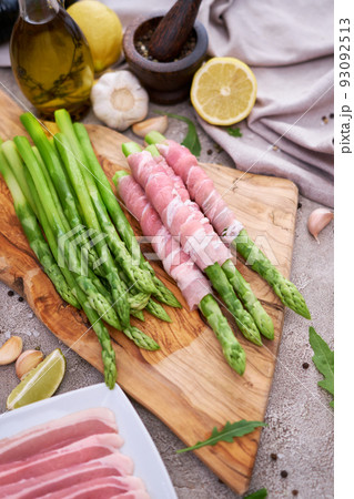 Green organic natural Asparagus on wooden cutting board and slice bacon at kitchen table Green organic natural Asparagus on wooden cutting board and slice bacon at kitchen table 93092513
