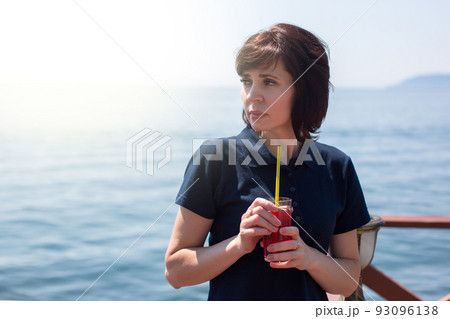 Pretty woman drinking fruit smoothie through a straw against the background of the sea 93096138