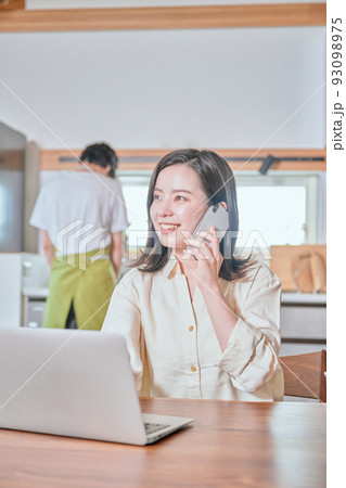 テレワークでスマホで電話をする女性と家事をする男性 テレワークでスマホで電話をする女性と家事をする男性 93098975