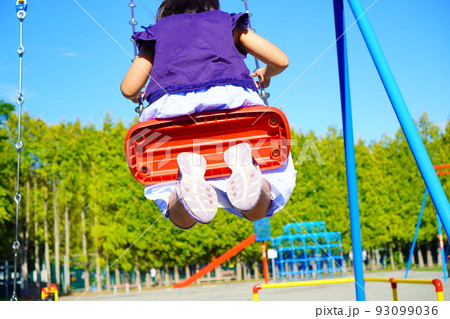 女の子が公園でブランコに乗っている後ろ姿。ブランコが大きく揺れる。夏休みの公園。 93099036
