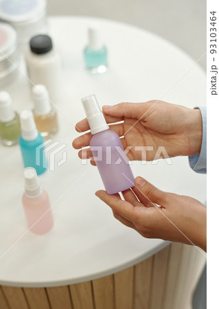 Hands of young woman holding small plastic bottle containing lilac liquid 93103464
