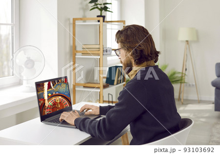 Caucasian man playing in online casino using laptop looking at monitor with roulette wheel 93103692