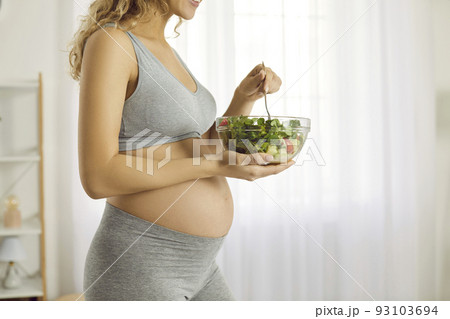 Bowl of green vegetable salad in hands of pregnant woman who monitors her diet during pregnancy. 93103694