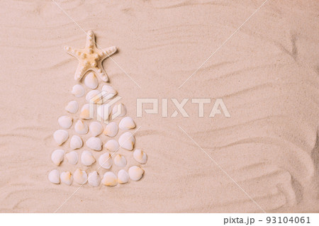 Creative Christmas tree made of shells background of sea sand. Concept tropical new year by the sea Creative Christmas tree made of shells background of sea sand. Concept tropical new year by the sea 93104061