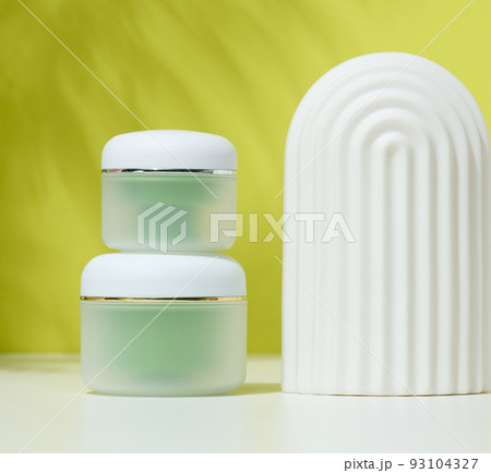 Green jar for cosmetics on a white table. Packaging for cream, gel, serum Green jar for cosmetics on a white table. Packaging for cream, gel, serum 93104327