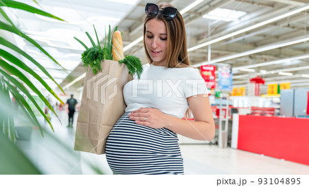 Pregnant healthy food bag. Pregnancy woman with healthy vegetables fresh, lettuce salad leaves in market food bag on grocery supermarket background. Healthy food background. 93104895