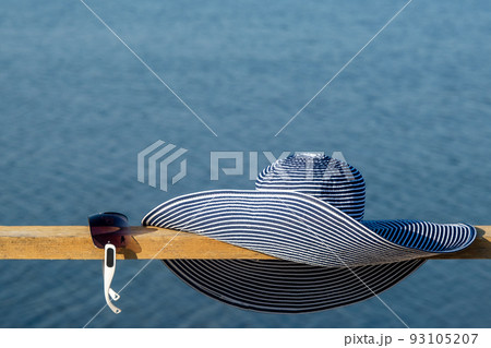 Women's blue sun hat. Sunglasses fashionable lie nearby. Against the backdrop of the blue sea. Blue sea background Women's blue sun hat. Sunglasses fashionable lie nearby. Against the backdrop of the blue sea. Blue sea background 93105207
