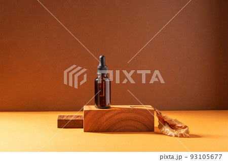 Cosmetic dropper bottle on a creative modern podium. Brown background with hard shadows, copy space 93105677