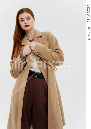Shooting for the outerwear catalog. Red-haired beauty in a beige full-length coat in the studio on a white background Shooting for the outerwear catalog. Red-haired beauty in a beige full-length coat in the studio on a white background 93106726