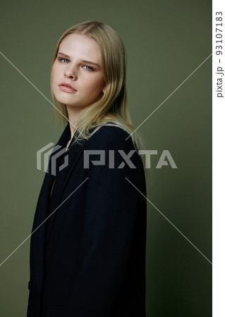 Blonde looks over her shoulder in a black jacket posing half-turned in the studio on a green background. The concept of stylish fashion photography Blonde looks over her shoulder in a black jacket posing half-turned in the studio on a green background. The concept of stylish fashion photography 93107183
