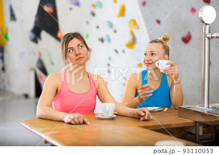 Two sports women drink tea or coffee after training on climbing wall 93110053