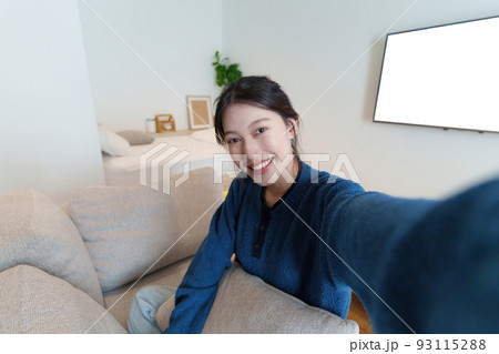 Portrait of Young Asian woman video call with her friend and checking social media by smartphone sitting on couch. Lifestlye concept. 93115288