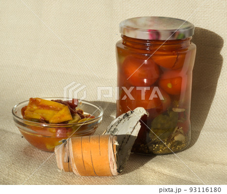 A jar of pickled tomatoes, a bowl of pickled hot peppers on a background of flax birch bark 93116180