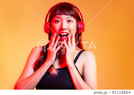 Young asian woman in black tank top wearing red headphones listen to music online on orange color background 93118904