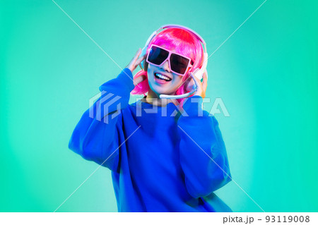 happy asian woman in blue sweatshirt pink short hair punk style wearing sunglasses and headphones dancing on the green background 93119008