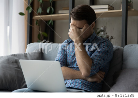 Upset man sit on sofa with laptop Upset man sit on sofa with laptop 93121239