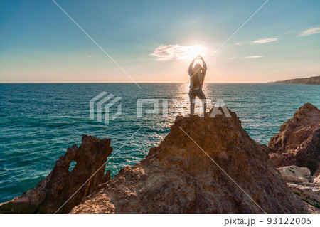 A female tourist, standing with her hands up, reaches the ends of the earth and sees the dragon rock. The girl welcomes the sun. Concept design. A successful woman looks at the sunset with open arms. 93122005