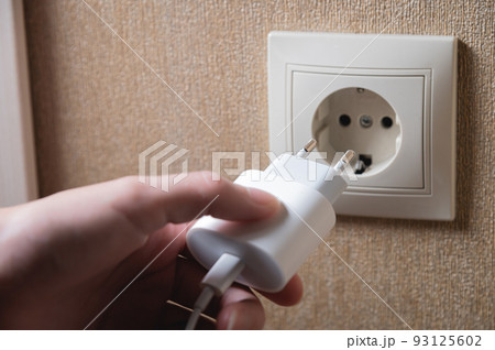 A young woman inserts a plug into a socket. A young woman plugs a charger or electrical appliance power cord into a socket. High quality photo A young woman inserts a plug into a socket. A young woman plugs a charger or electrical appliance power cord into a socket. High quality photo 93125602