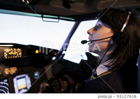 Female copilot flying plane from cockpit with dashboard command and control panel, using steering wheel and control panel for windscreen navigation. Woman using lever to fly aircraft. Female copilot flying plane from cockpit with dashboard command and control panel, using steering wheel and control panel for windscreen navigation. Woman using lever to fly aircraft. 93127616