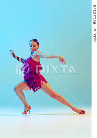Fiery dance. Young graceful flexible woman dancing ballroom dance without partner isolated on blue background in neon light. Concept of art, beauty Fiery dance. Young graceful flexible woman dancing ballroom dance without partner isolated on blue background in neon light. Concept of art, beauty 93128128