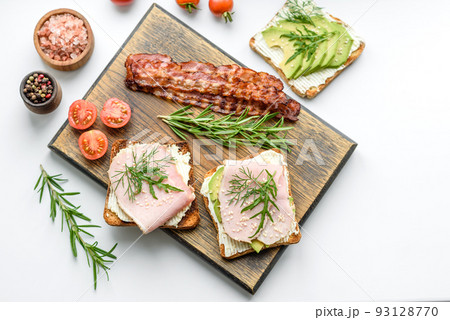 Fresh, delicious ham, butter, avocado and sesame seeds sandwiches on a wooden cutting board Fresh, delicious ham, butter, avocado and sesame seeds sandwiches on a wooden cutting board 93128770